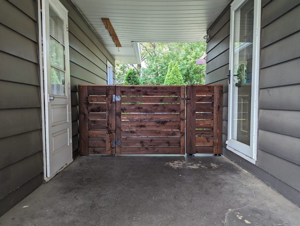 A cedar wooden fence gate on the porch of a home with a Perfect Picket Fence & Stain.