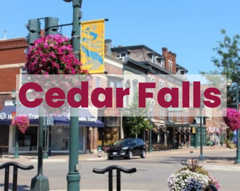 Bustling Cedar Falls street with red-brick buildings, flower baskets, lampposts, and parked cars.