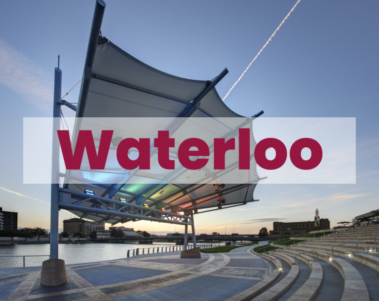 Modern amphitheater with canopy by waterfront, "Waterloo" text overlay, twilight sky, buildings background