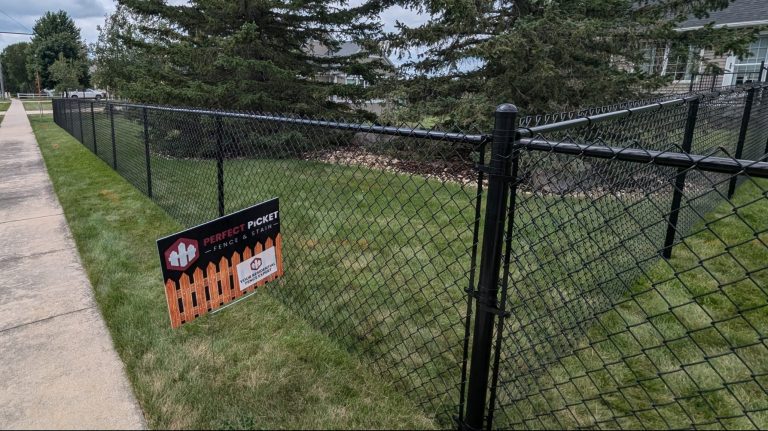 Black chain link fence installation along a sidewalk with a Perfect Picket Fence and Stain sign in Waterloo, Iowa