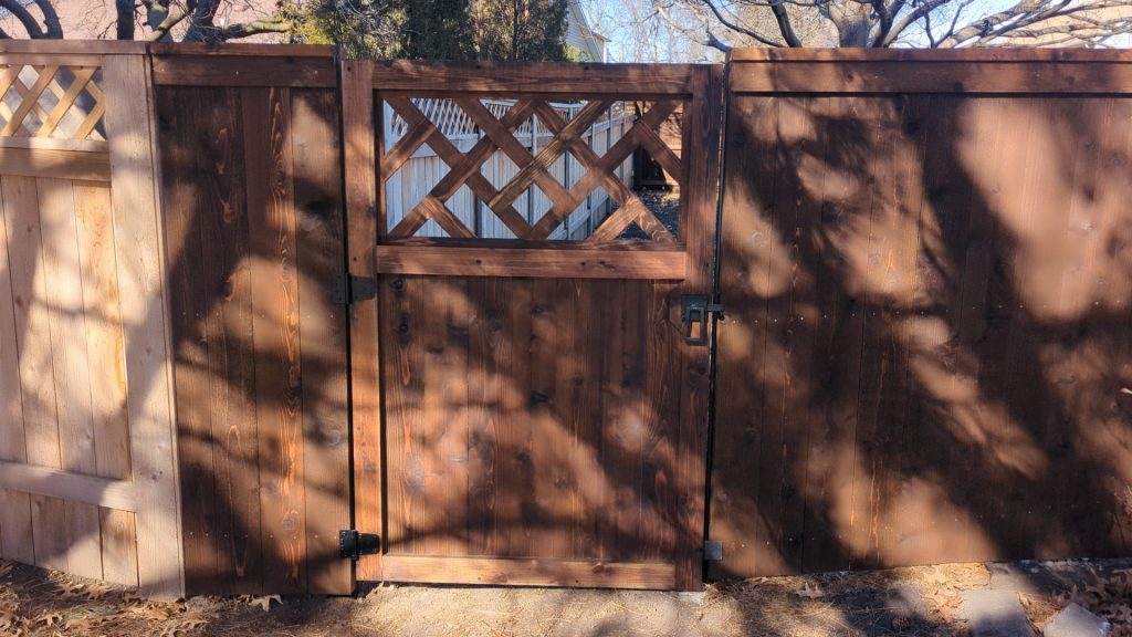 Wooden gate with lattice top, set in wooden fence, metal latch and hinges, shaded by trees